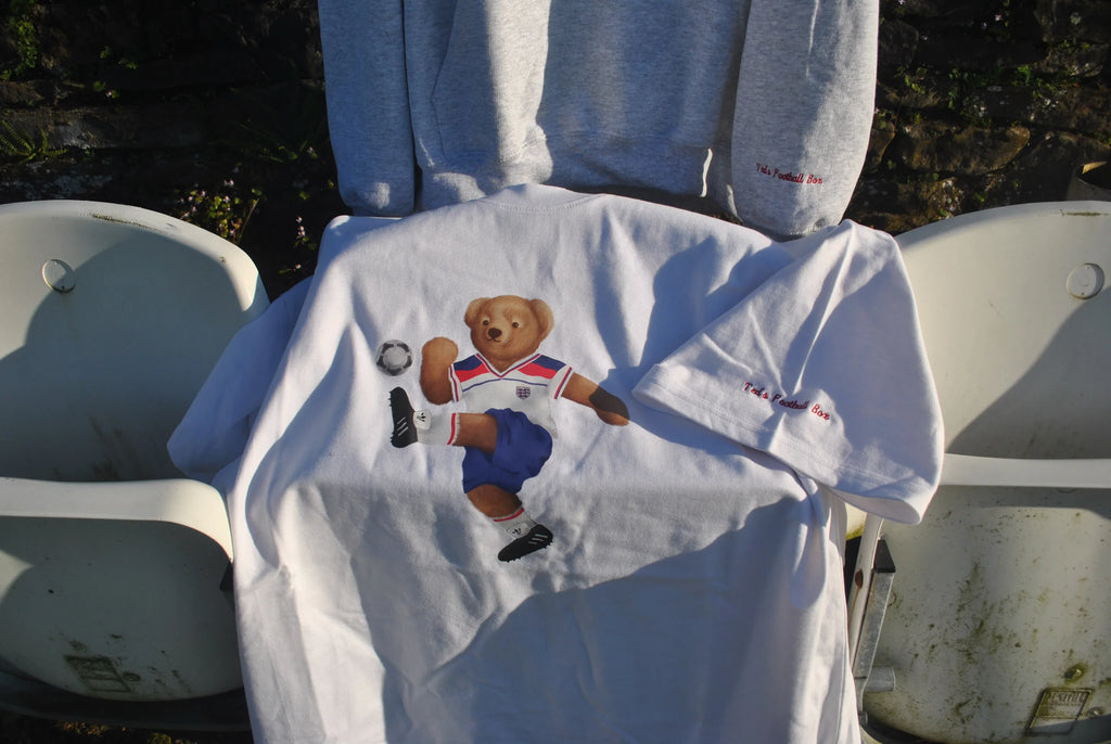 White t-shirt with a bear graphic and text draped over a chair outdoors