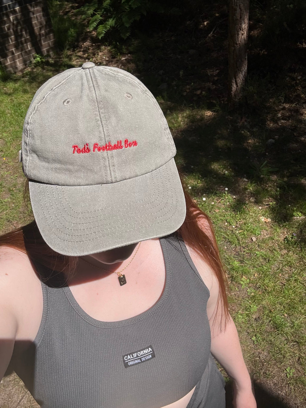 Person wearing a gray cap with red text and a gray tank top with 'teds football box' text, standing outdoors.