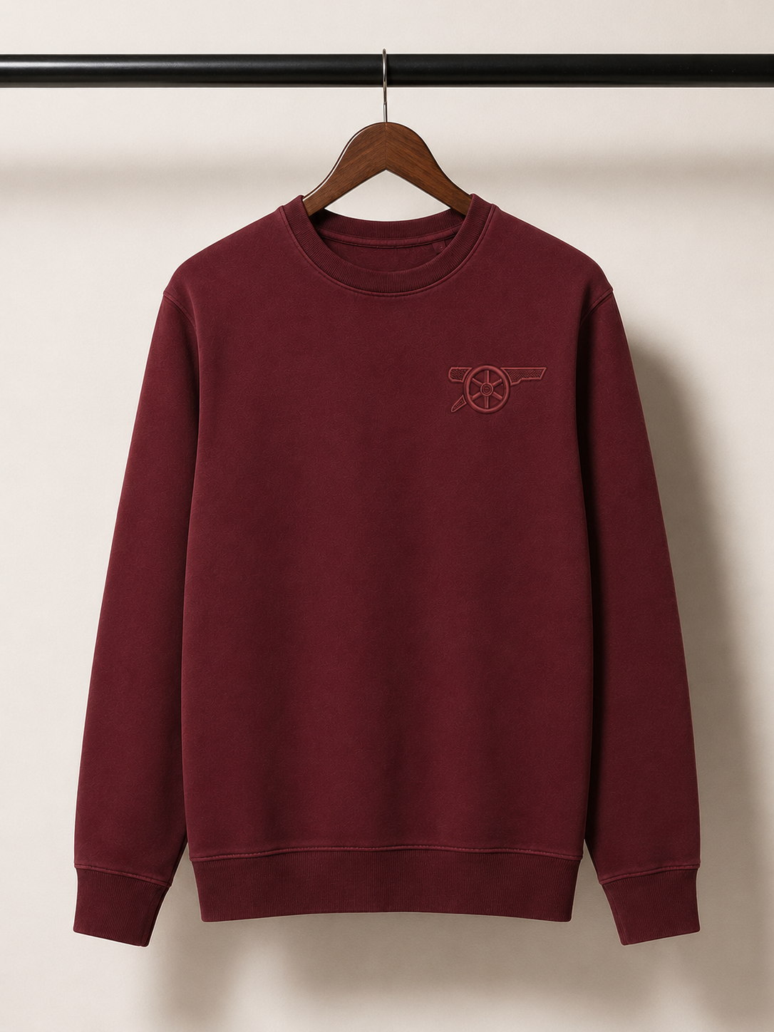 Maroon sweatshirt with a logo on a hanger against a plain background