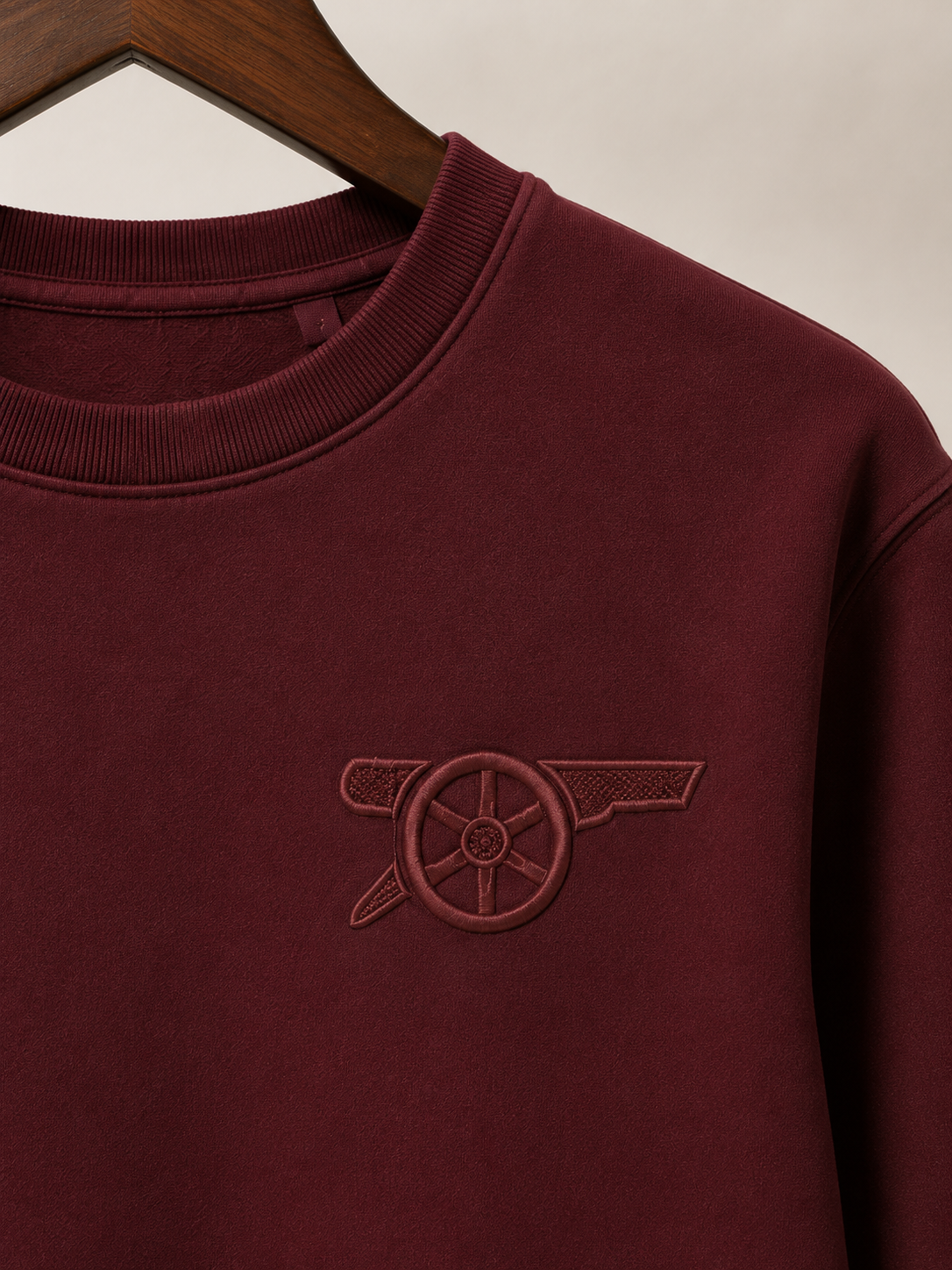 Maroon sweatshirt with embroidered logo on a beige background