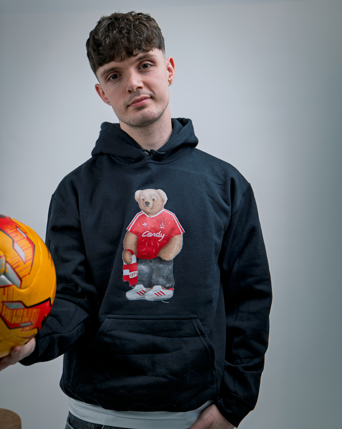 Person wearing a black hoodie with a bear graphic holding a helmet, on a gray background