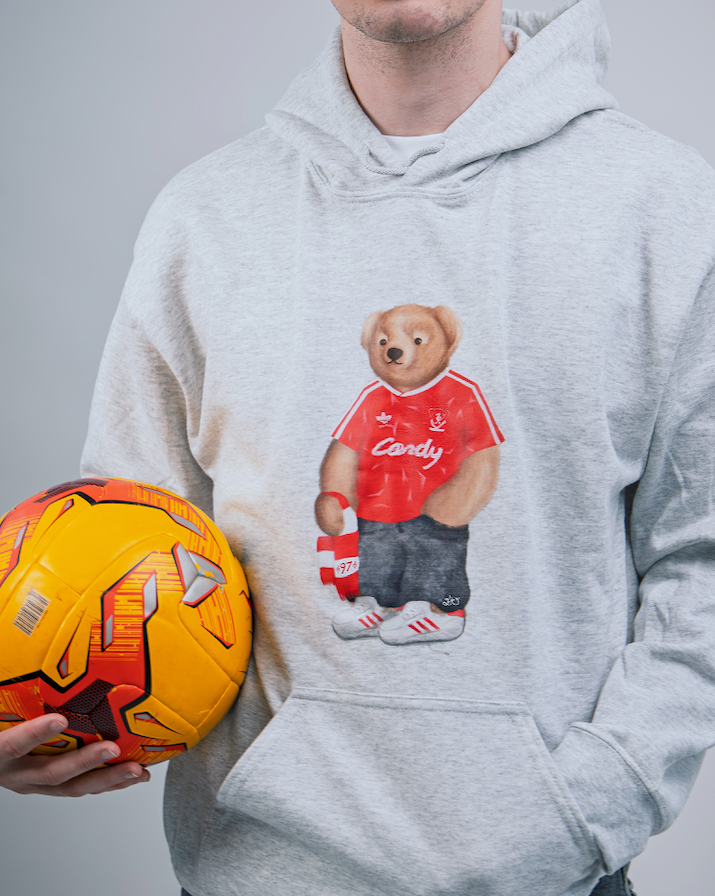 Person wearing a hoodie with a bear graphic holding a soccer ball.