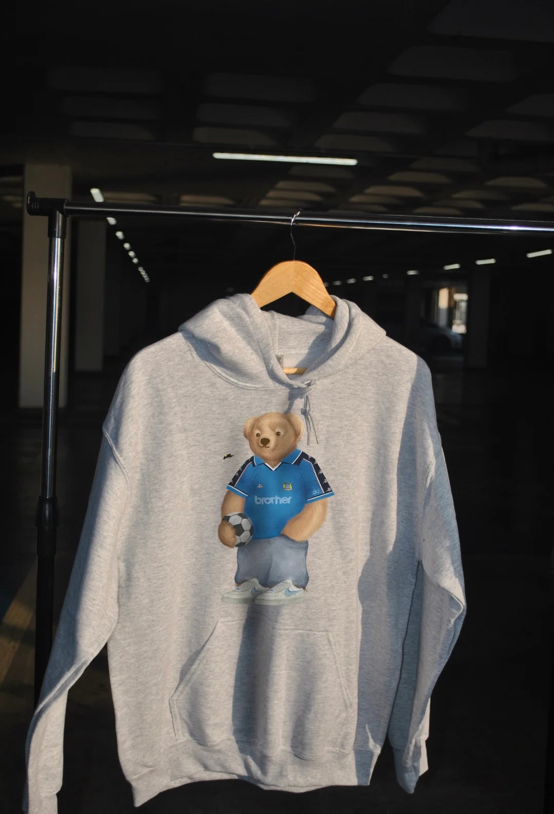 Gray hoodie with a bear graphic on a hanger against a dark background