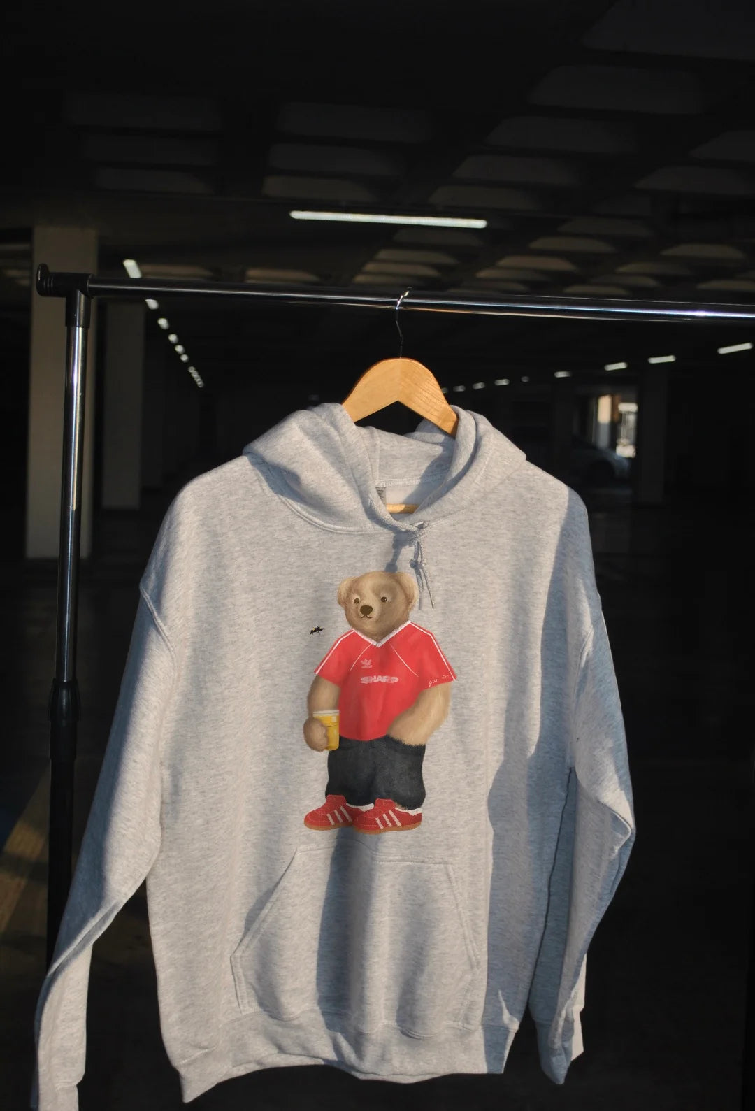 Gray hoodie with a bear graphic in red shirt and black shorts on a hanger against a dark background.