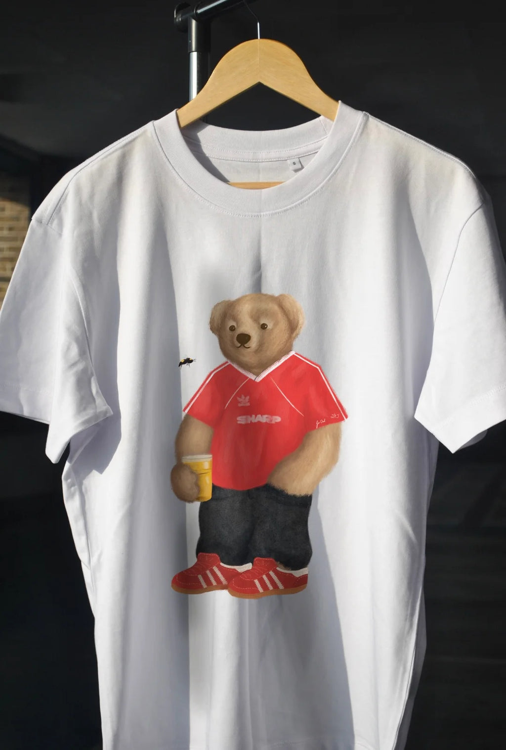 White t-shirt with a bear graphic wearing a red shirt and black pants on a hanger.