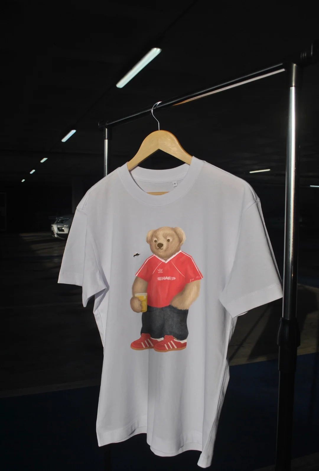 White t-shirt with a bear graphic wearing a red shirt and black pants on a hanger against a dark background.