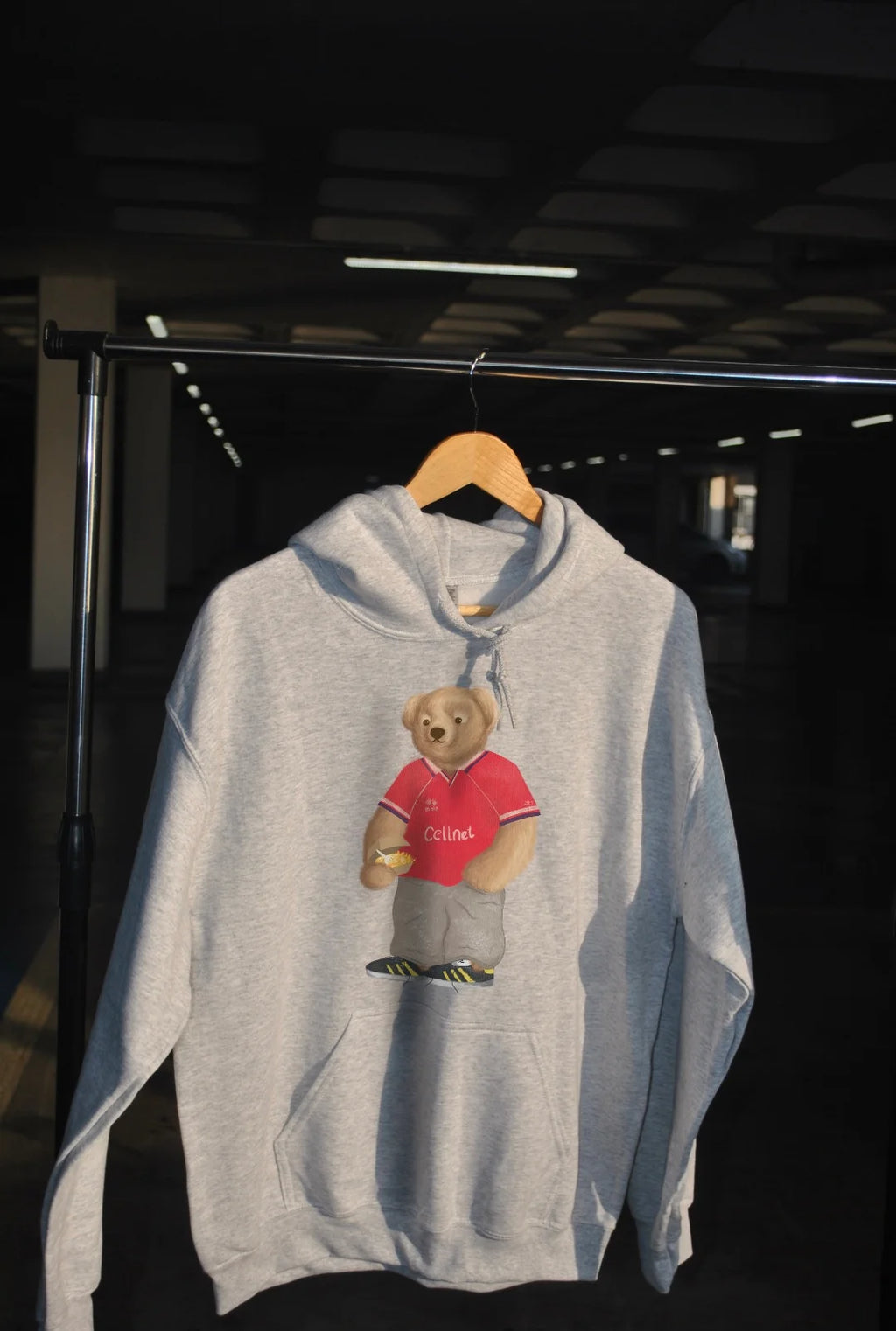 Gray hoodie with a teddy bear graphic on a hanger against a dark background