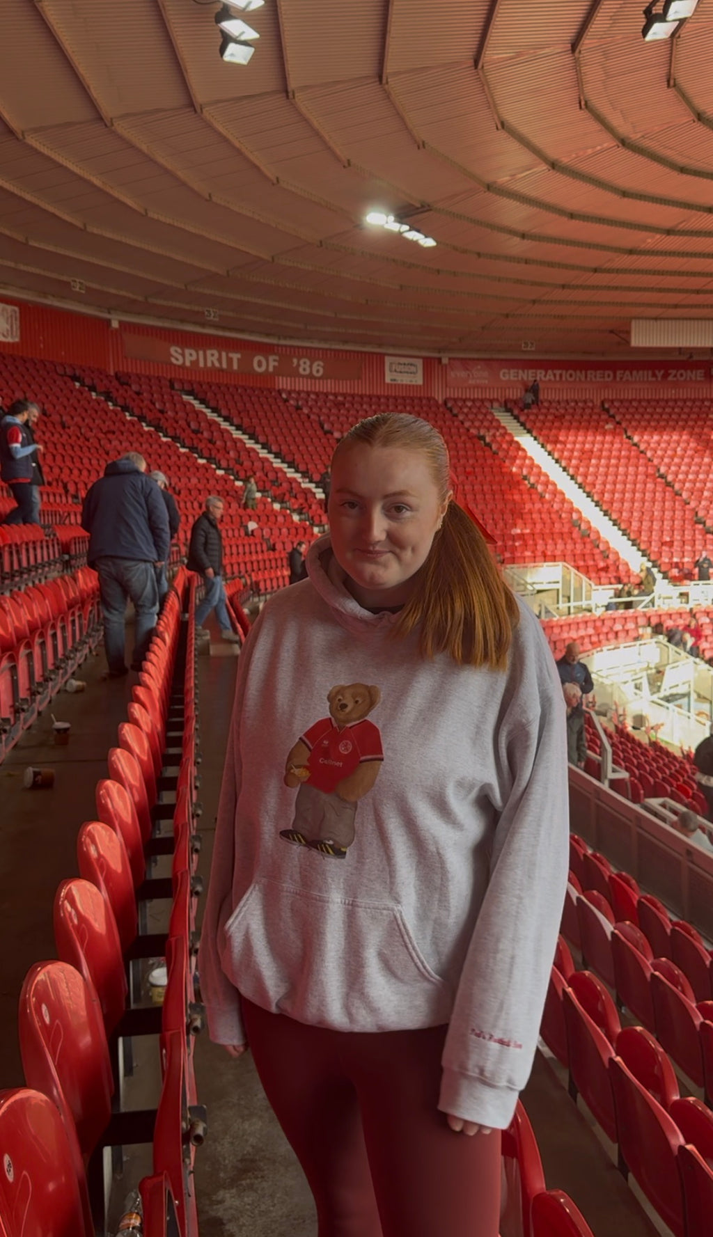 Person wearing a white hoodie with a teddy bear graphic in an indoor stadium setting