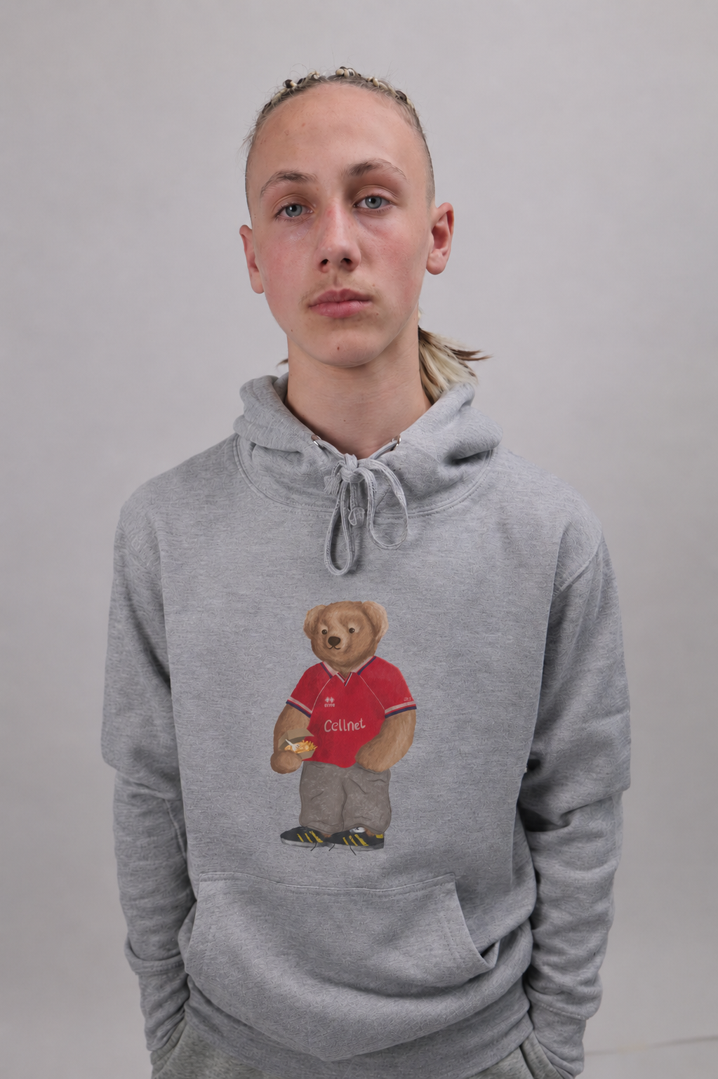A person wearing a light gray pullover hoodie with a teddy bear graphic on the chest, standing against a plain light gray background.