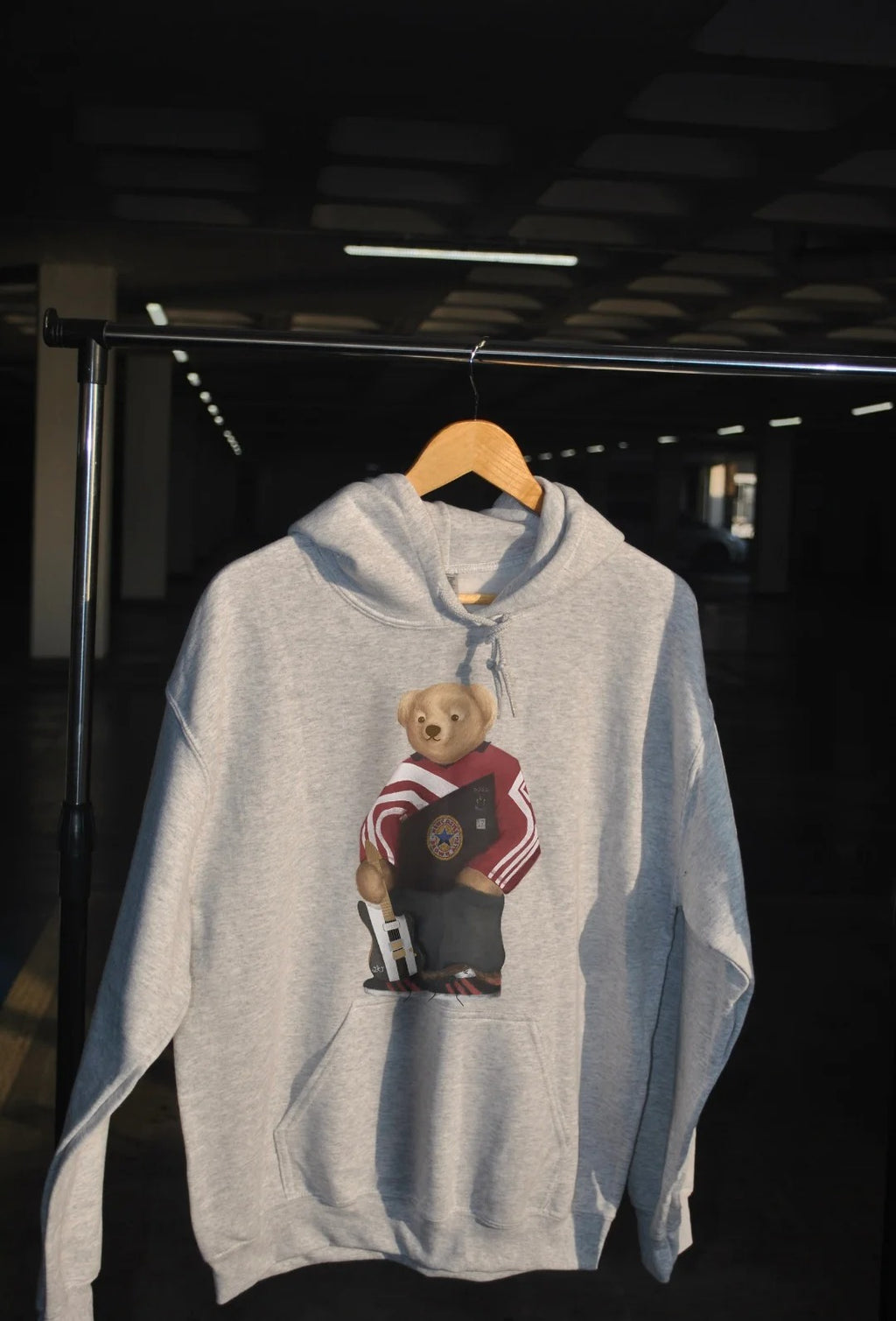 Gray hoodie with bear graphic on a wooden hanger against a dark background