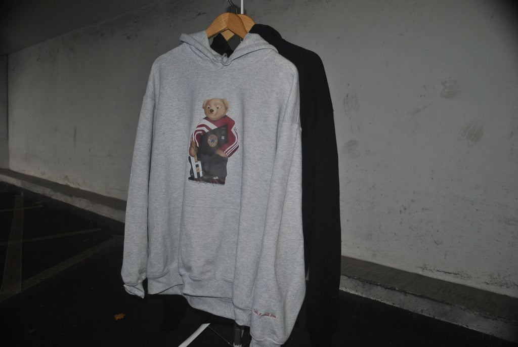 Gray hoodie with a bear graphic on a hanger against a plain wall.