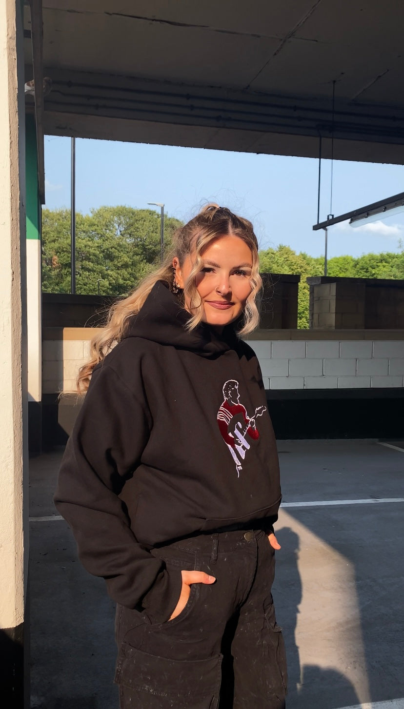 Person wearing a black hoodie with a graphic design, standing outdoors.