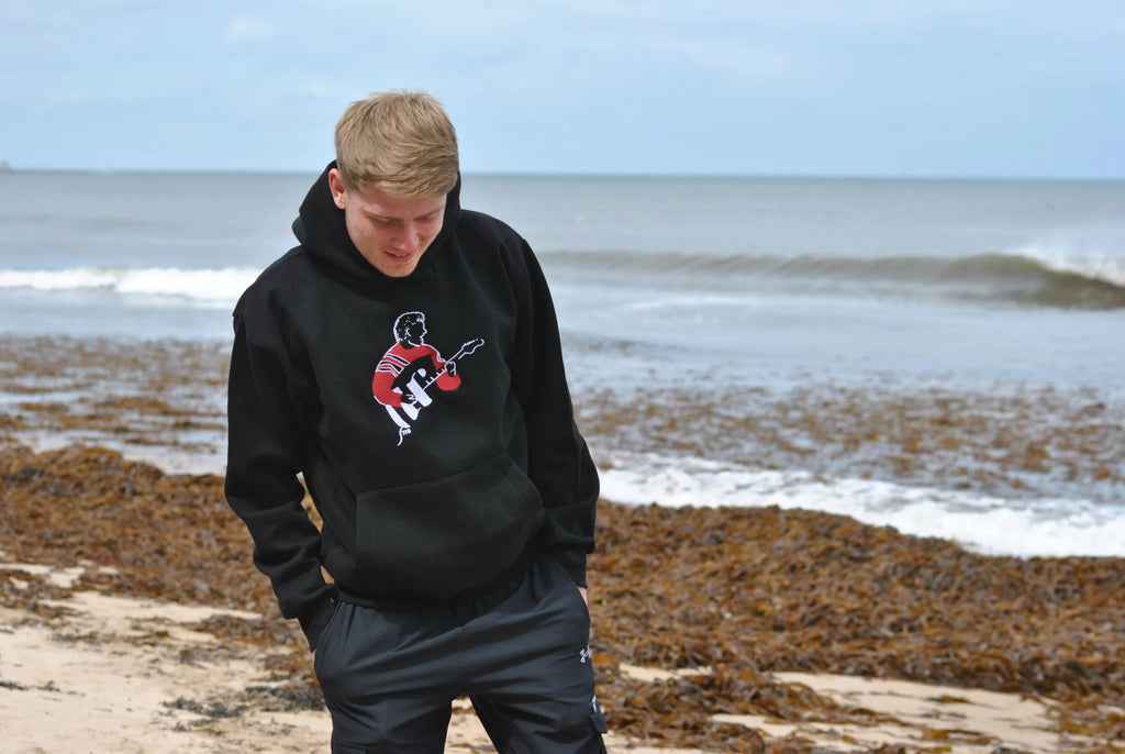 Person wearing a black hoodie with a graphic design on a beach