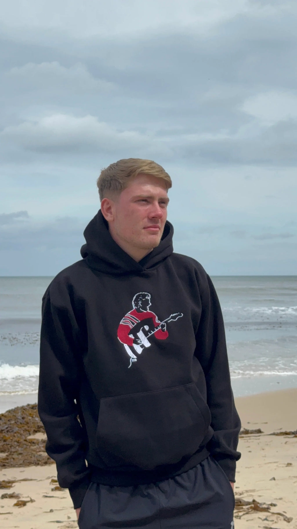 Person wearing a black hoodie with a graphic design on a beach
