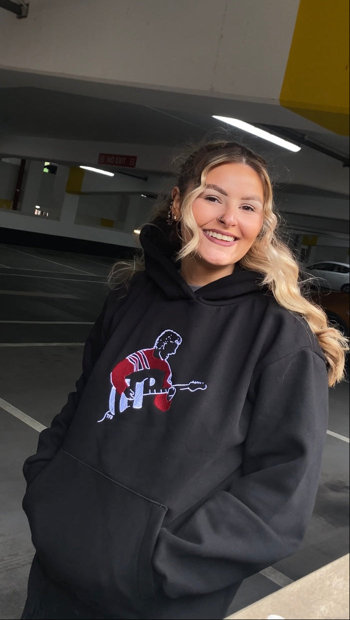 Person wearing a black hoodie with a colorful graphic in an indoor parking garage.