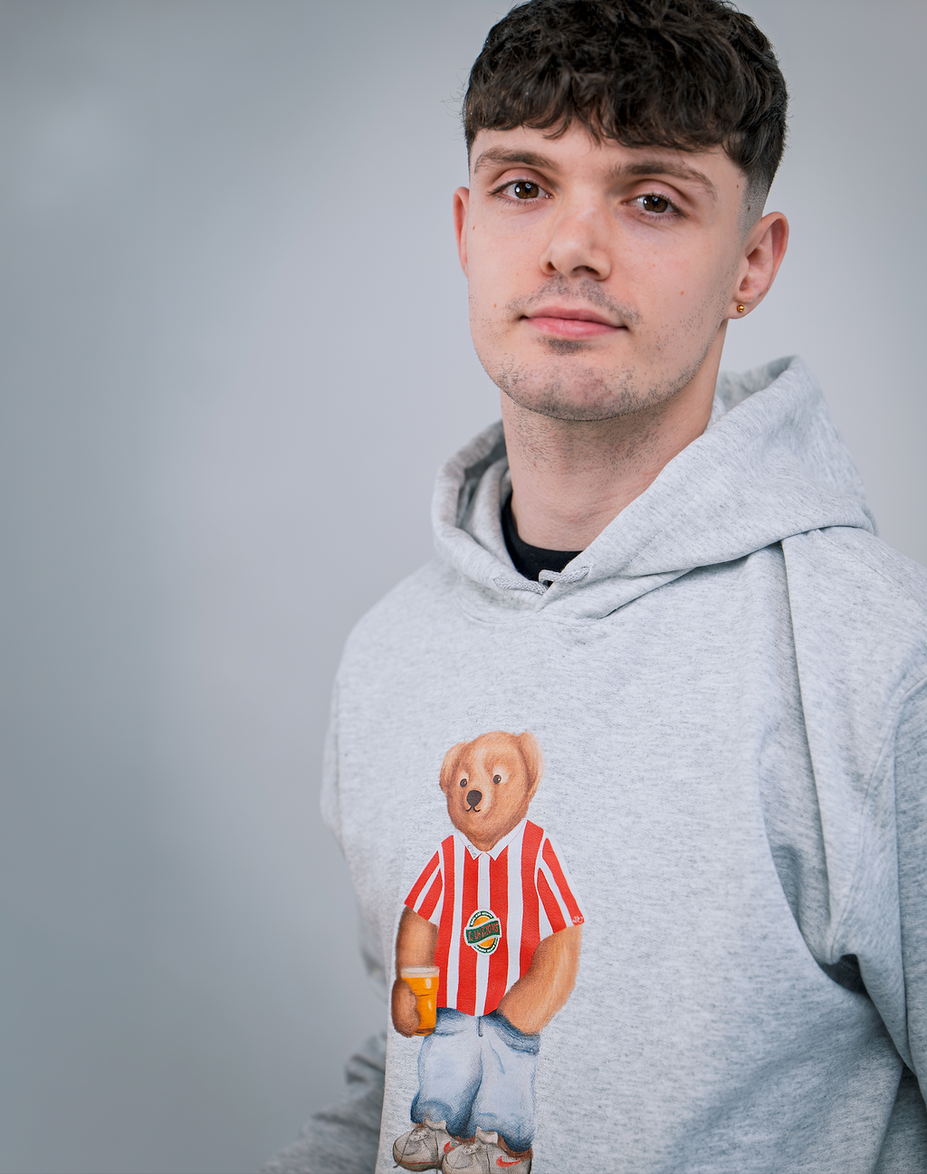 Man wearing a gray hoodie with a bear graphic on a plain background
