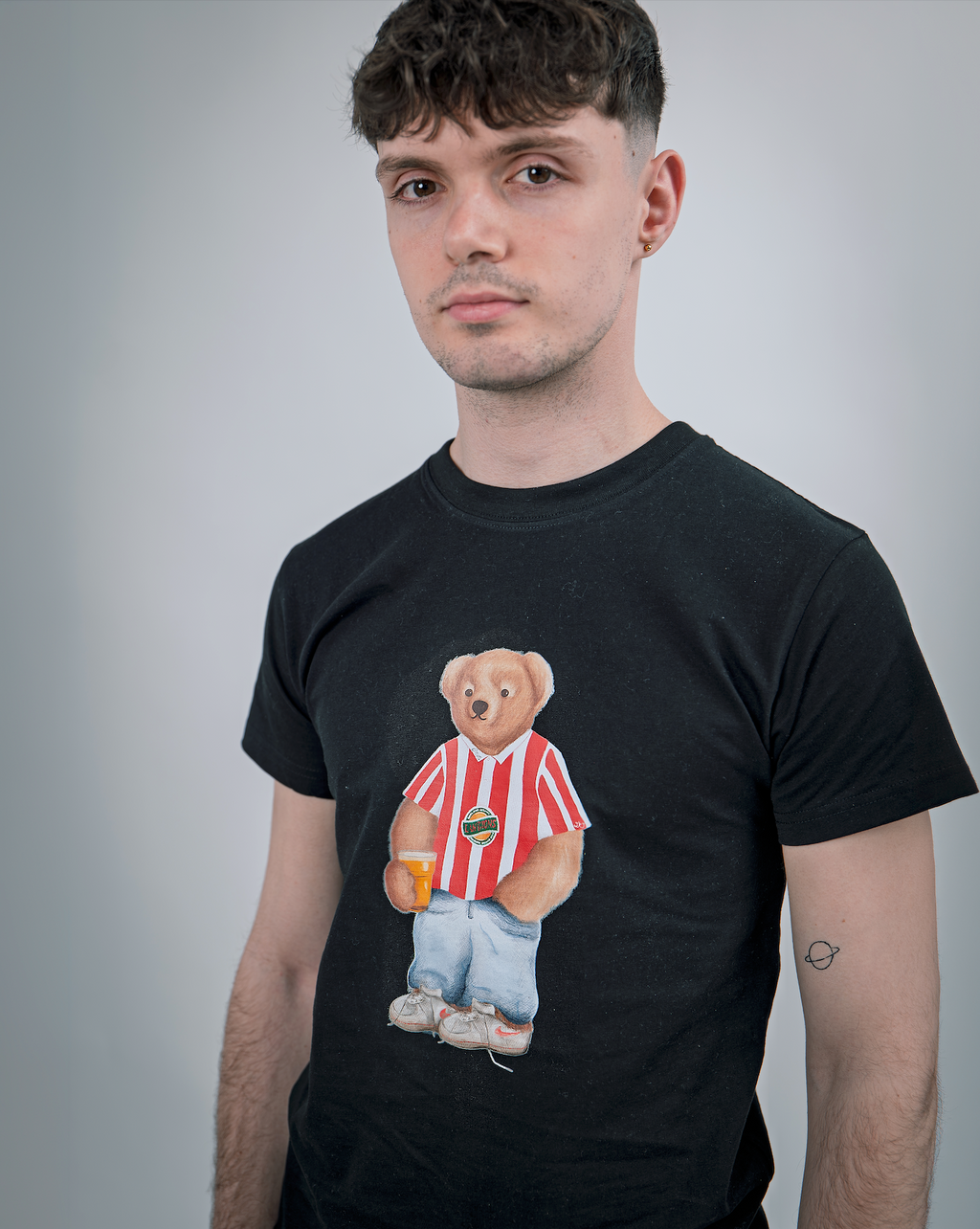 Person wearing a black t-shirt with a teddy bear graphic holding a beer.