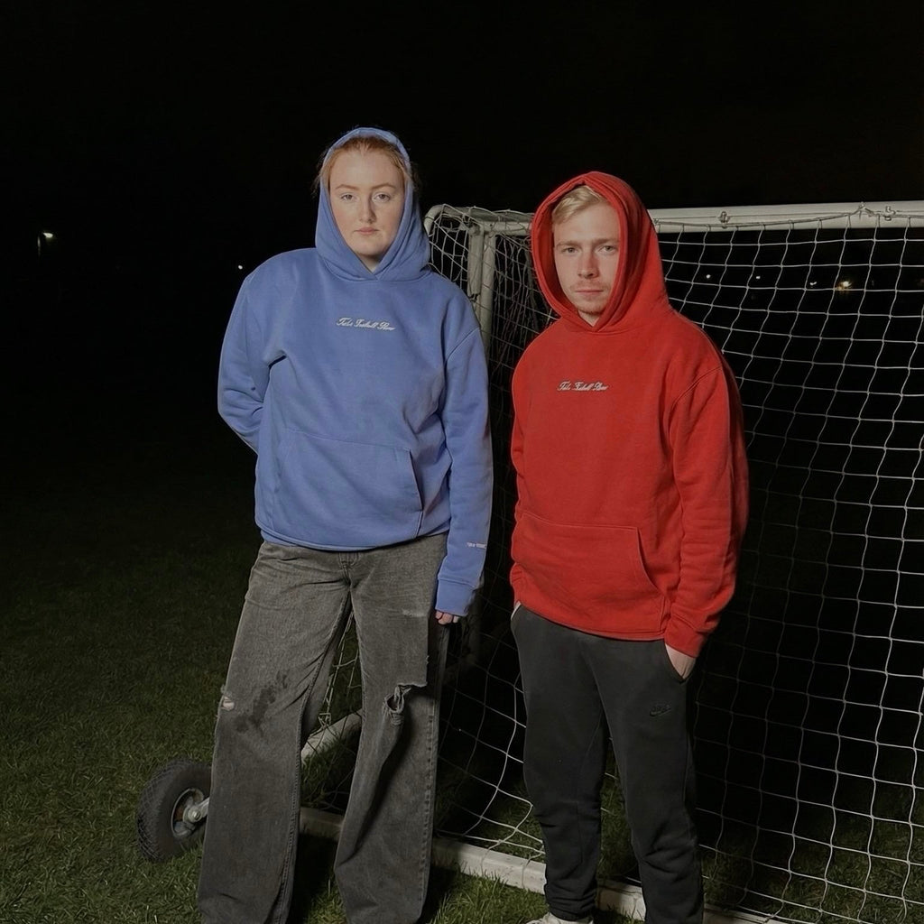 Two people wearing hoodies standing in front of a soccer goal at night.