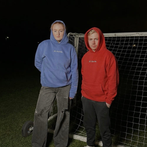 Two people wearing hoodies standing in front of a soccer goal at night.