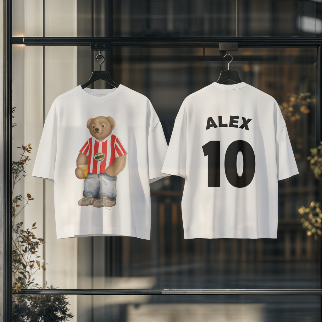 Two white t-shirts with a teddy bear graphic and text 'ALEX 10' displayed against a blurred indoor background.