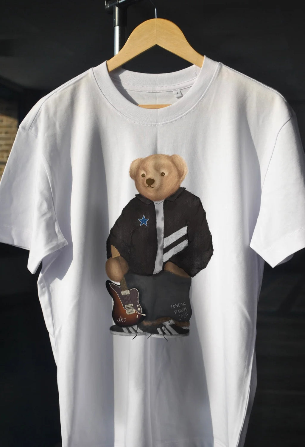 White t-shirt with a bear graphic on a hanger against a dark background