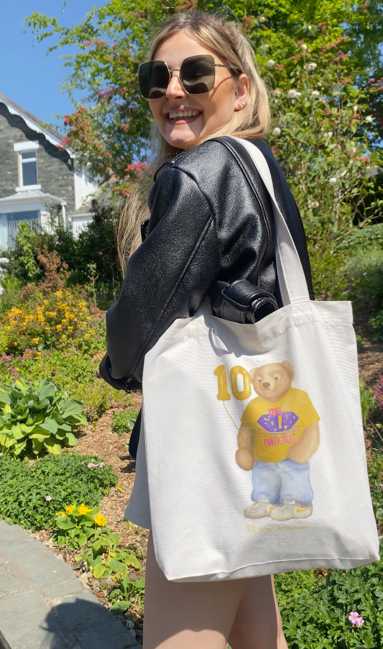 Person holding a tote bag with a graphic design of a bear and text, standing outdoors.