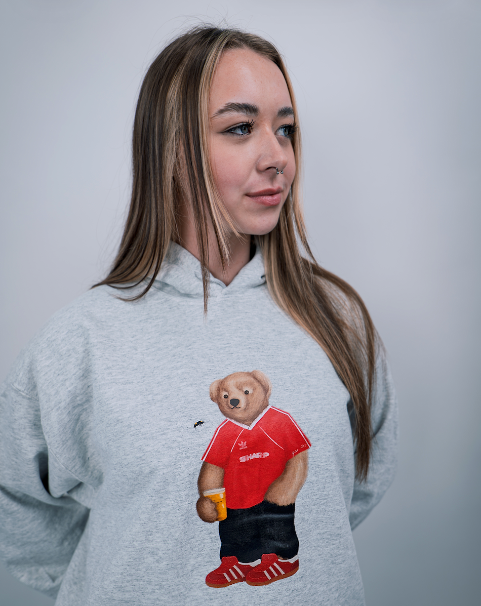 Person wearing a hoodie with a bear graphic holding a red shirt on a plain background