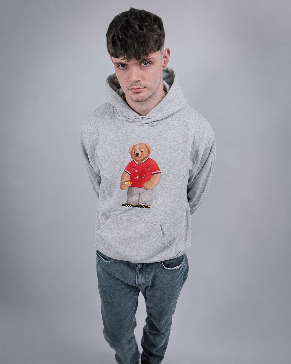 Person wearing a gray hoodie with a teddy bear graphic on a plain background