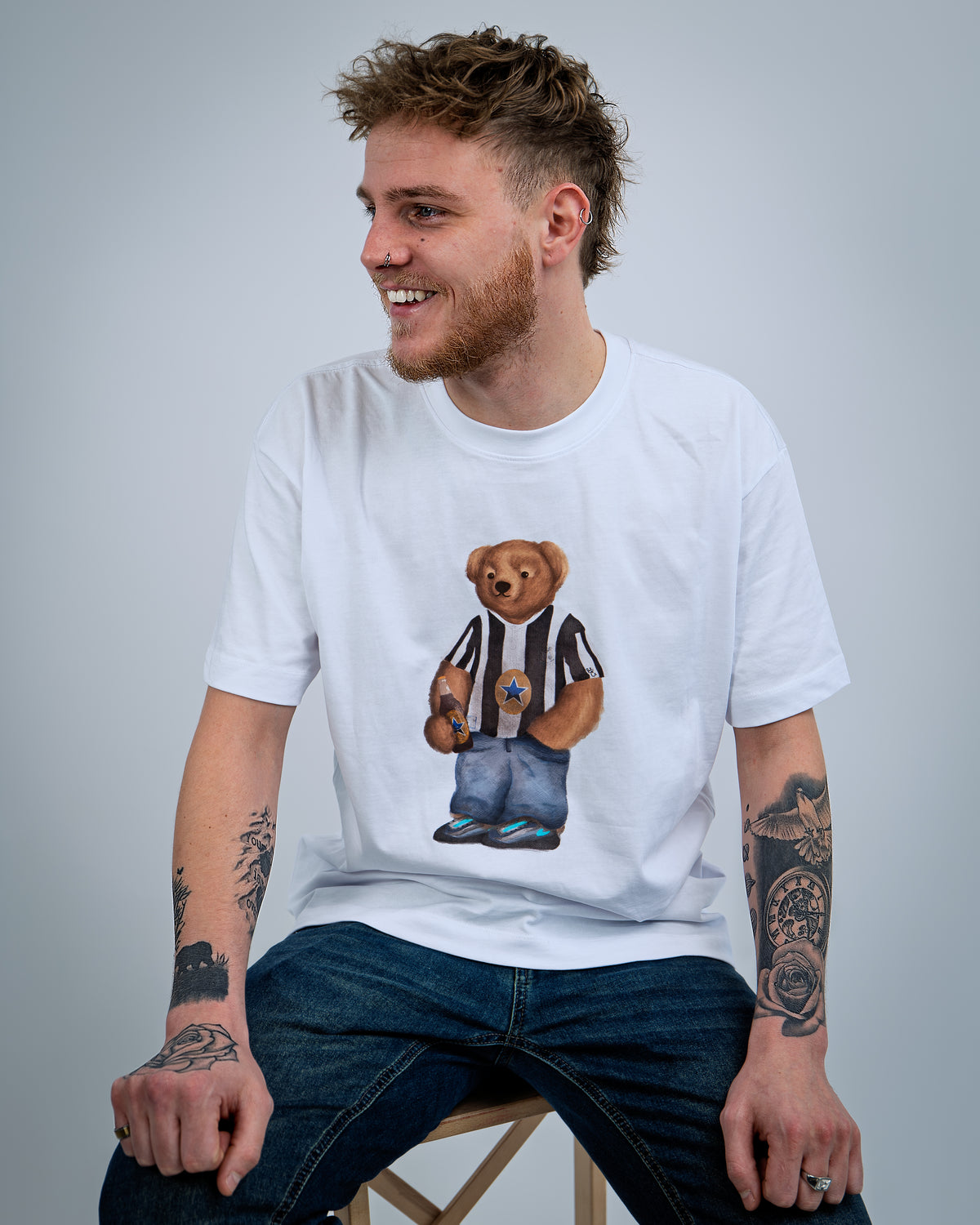 Man wearing a white t-shirt with a teddy bear graphic, sitting against a plain background