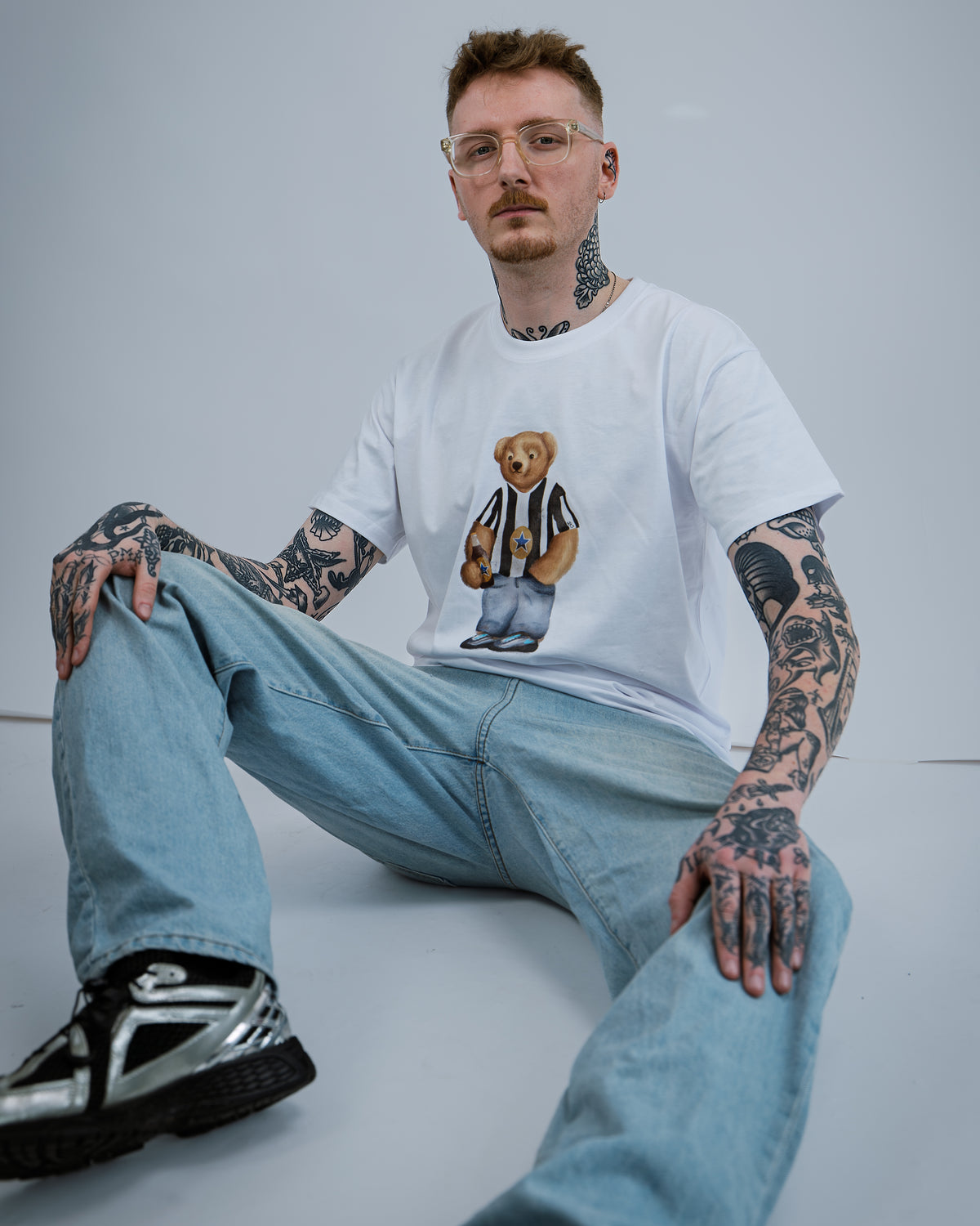 Man wearing a white t-shirt with a bear graphic and text, sitting on a light gray background.