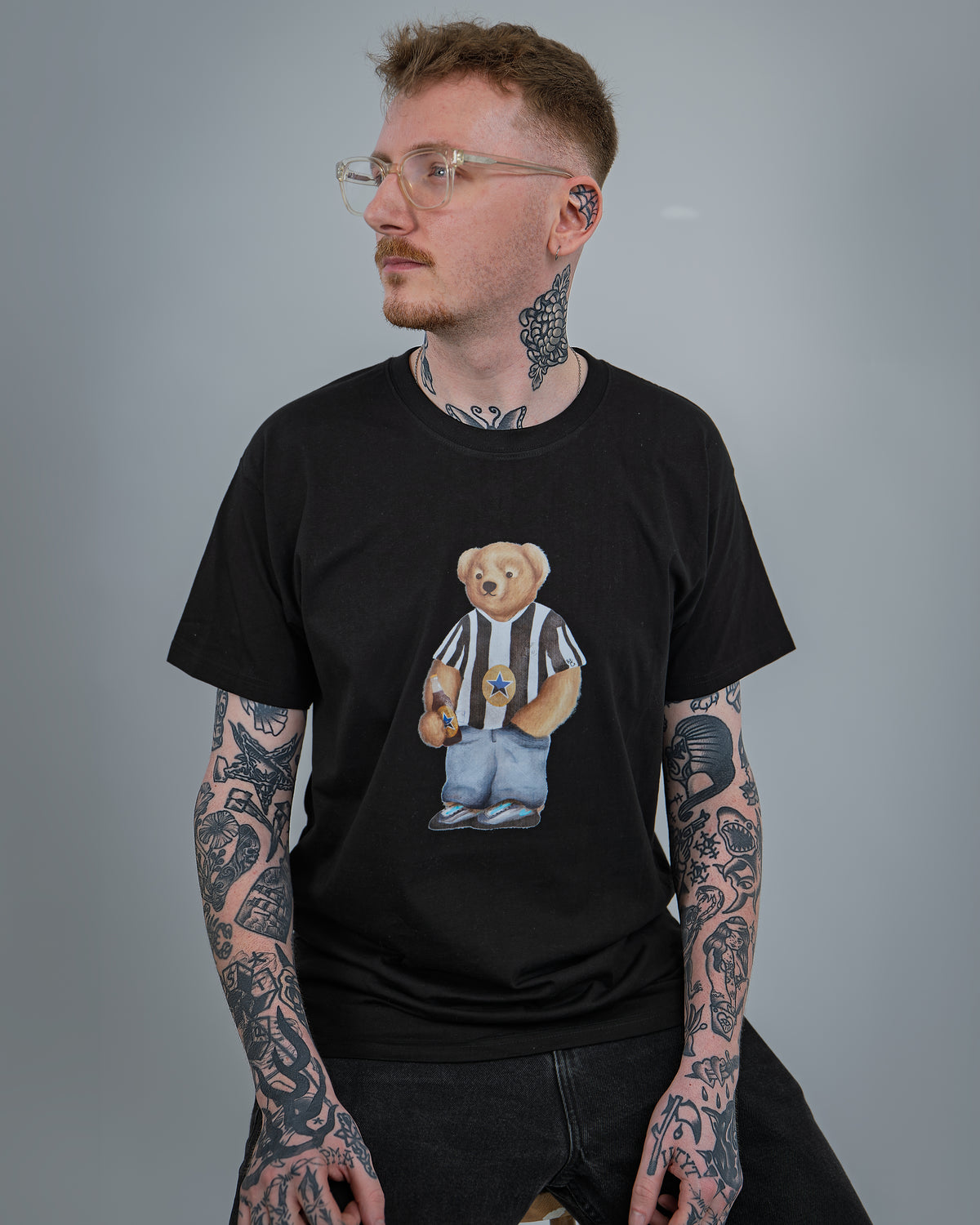 Man wearing a black t-shirt with a graphic of a bear in a striped shirt on a gray background