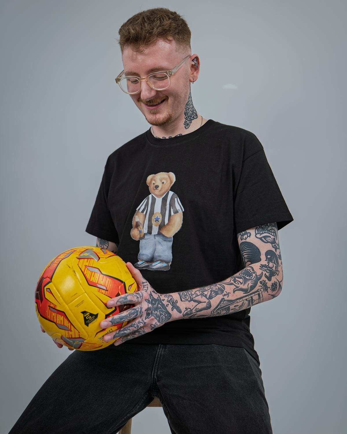 Man holding a yellow and red ball wearing a black t-shirt with a bear graphic.