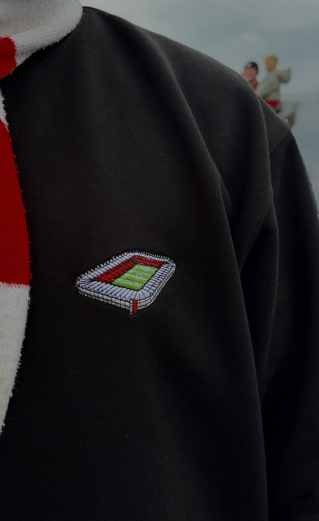 Black sweater with a small embroidered design on the chest against a blurred background