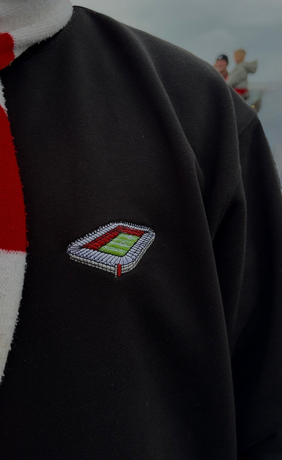 Black sweater with a small embroidered design on the chest against a blurred background